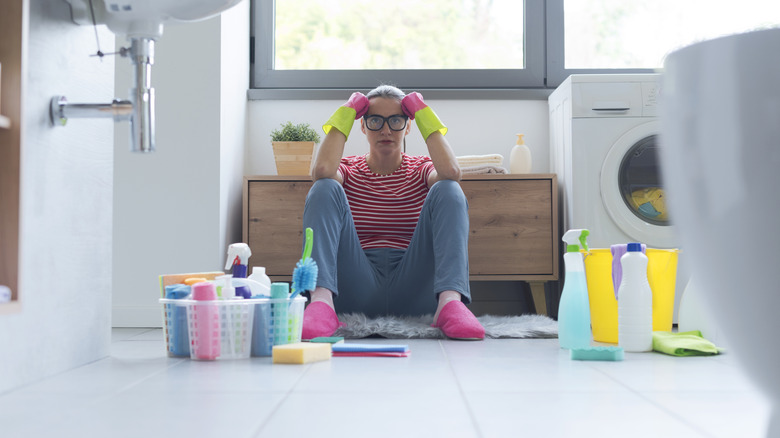 Frustrated woman sitting on bathroom floor with cleaning supplies