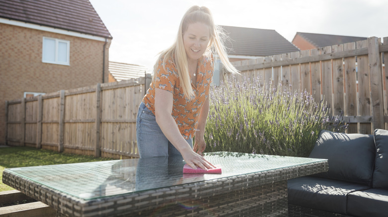 woman wiping down outdoor table with sponge in backyard
