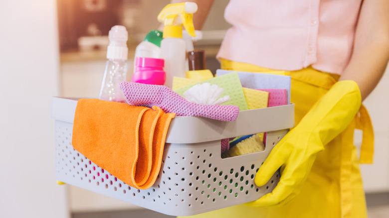 Person holding basket of various cleaning supplies