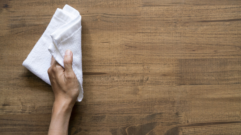A hand wiping a white cloth across wood surface