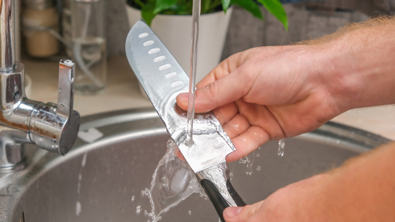 A man hand-washing a steel kitchen knife in the sink