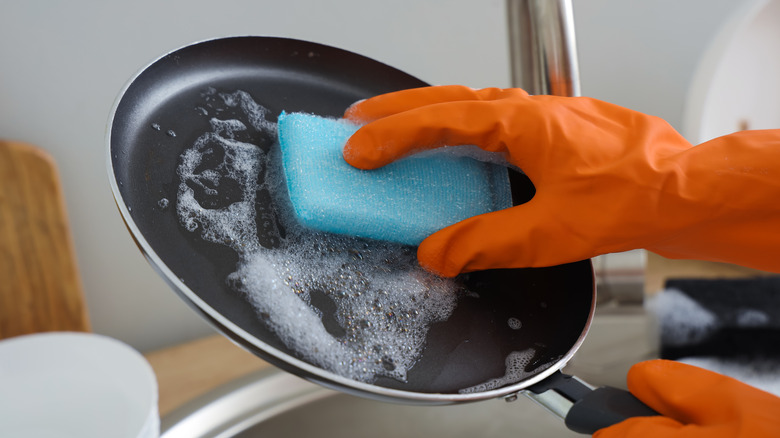 Someone handwashing a black nonstick pan.
