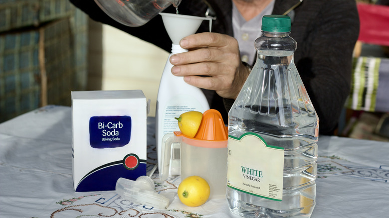 Someone adding vinegar to spray next to baking soda and lemon.