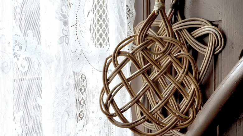 Two rattan carpet beaters hanging next to a window covered with a pretty lace curtain.