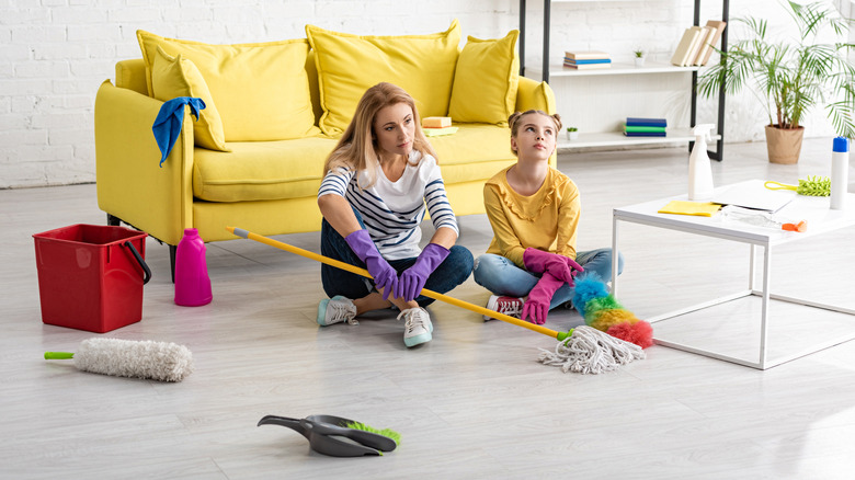 tired mother and daughter holding cleaning tools