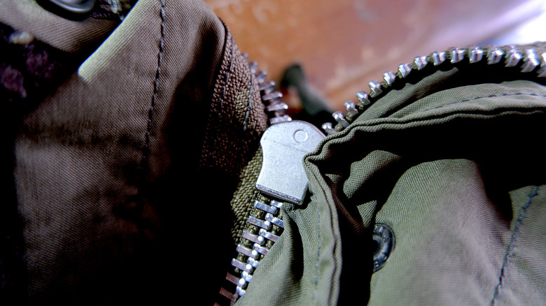 Close up of person holding back panel of zipper on jacket.