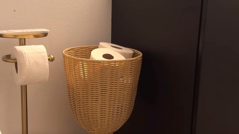 A stylish wicker planter holds toilet paper rolls next to the bathroom sink