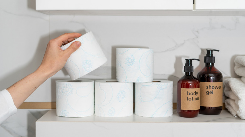 A person grabs a roll of toilet paper from a stack placed on a bathroom countertop