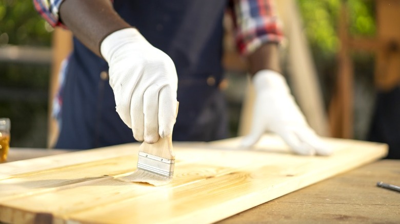 Person in white gloves brushing light stain onto pine boards