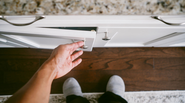 A man opening a white cabinet with silver knobs