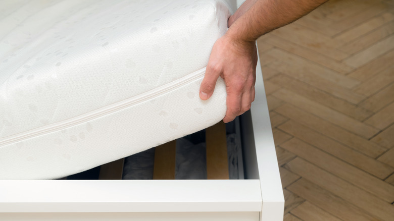 Close-up of a person lifting up a mattress from the bed frame