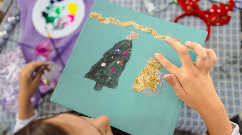 A girl making a Christmas card with messy glitter
