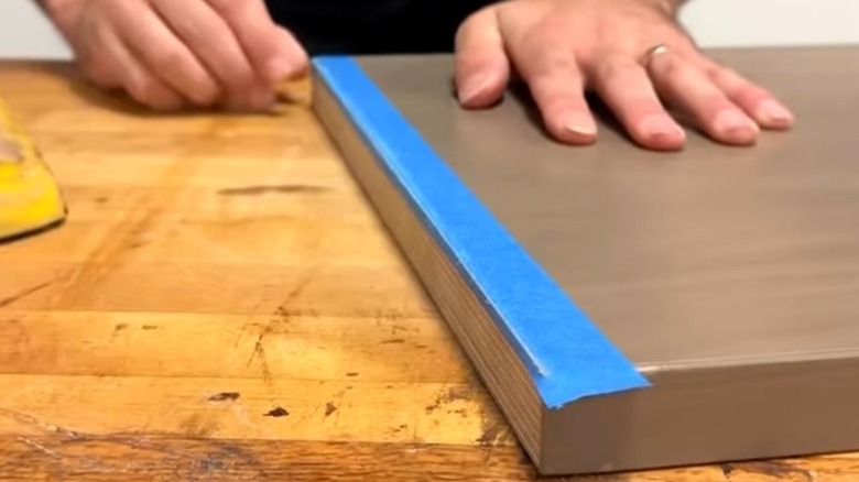 Person removing sanded off edge of painter's tape to make a cleanly taped wood edge