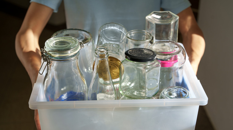 A person carries multiple washed and empty jars in a large plastic bin.
