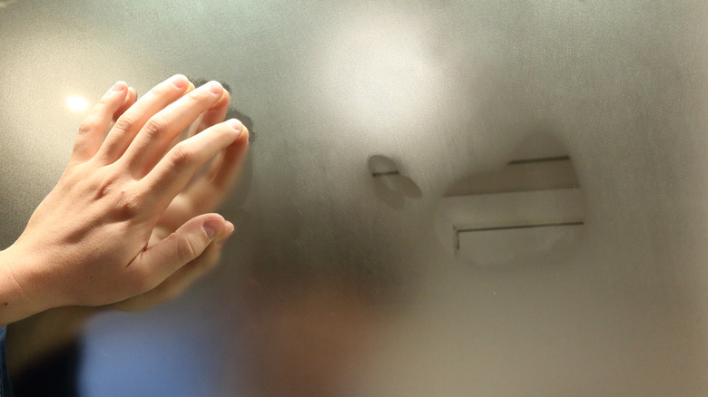 Hand touching a foggy bathroom mirror