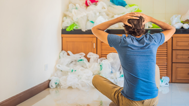 A man with too many plastic bags for his cabinet