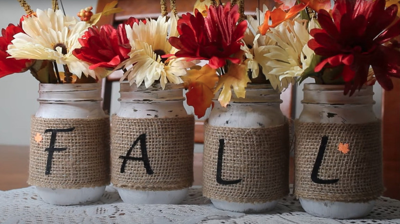 Glass jars adorned in fall decor with cream and red flowers