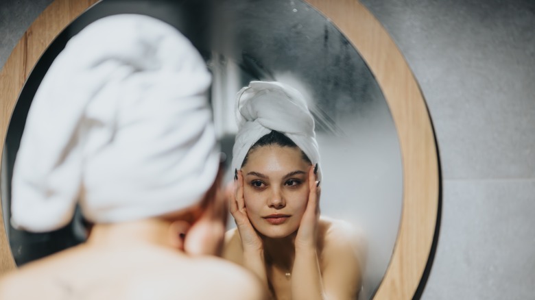 A woman stands in front of a foggy mirror in her bathroom