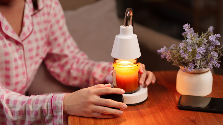 A woman places a candle under a white electric candle warmer lamp.