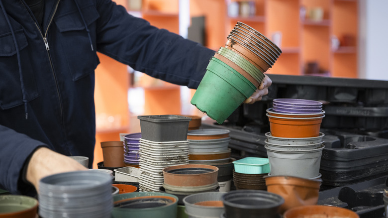 Person holding stacked plastic nursery pots in all colors
