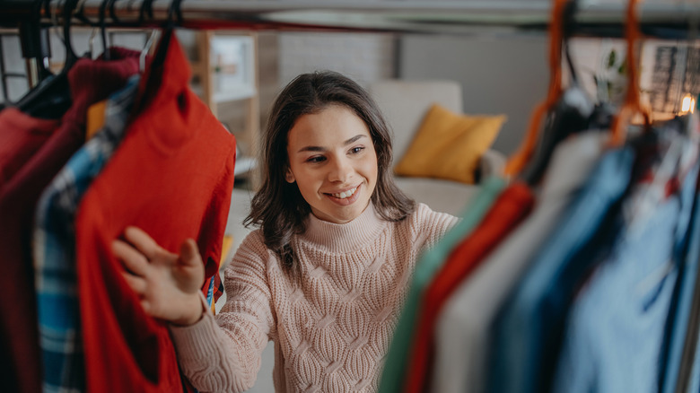 Young woman looking through clothes hanging in a wardrobe