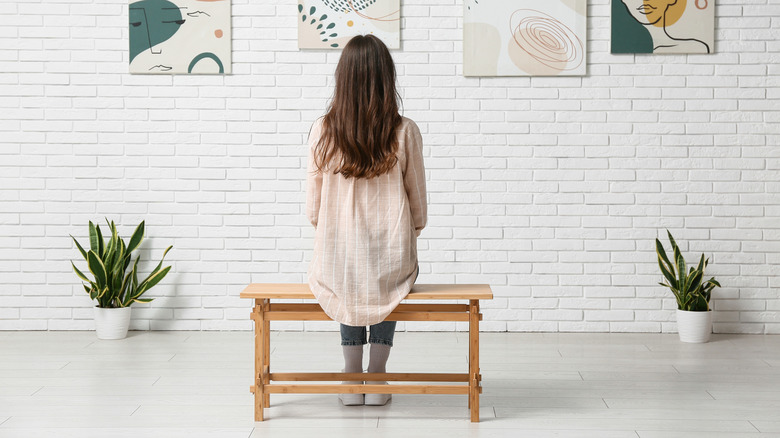 a woman sitting on a wooden bench looking at art
