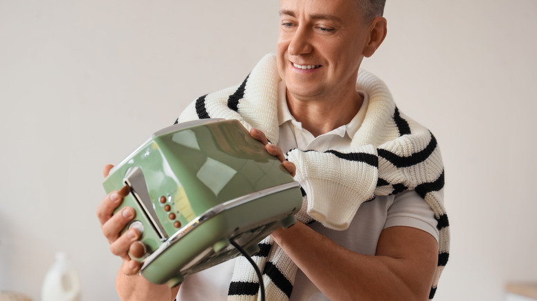 Caucasian man in white and black striped sweater tied around his neck holds green toaster