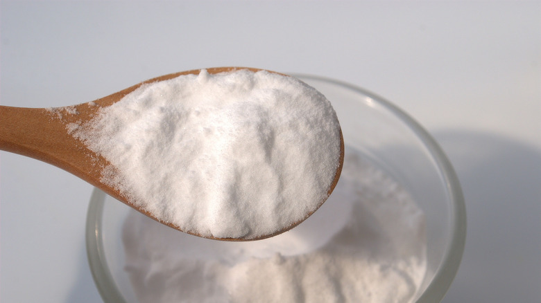 Wooden spoon scooping baking soda from a container