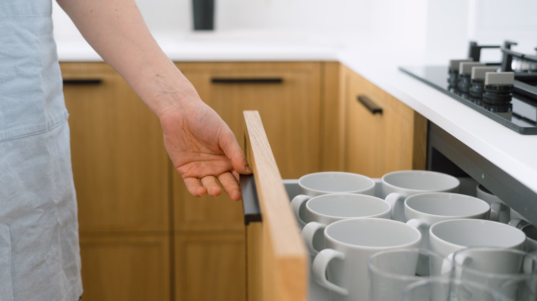 Person opening a drawer full of organized drinkware
