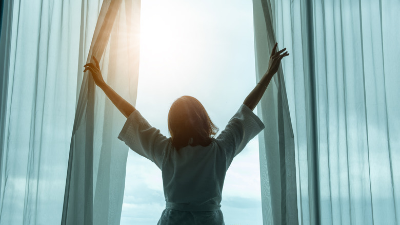 A woman opening large window curtains