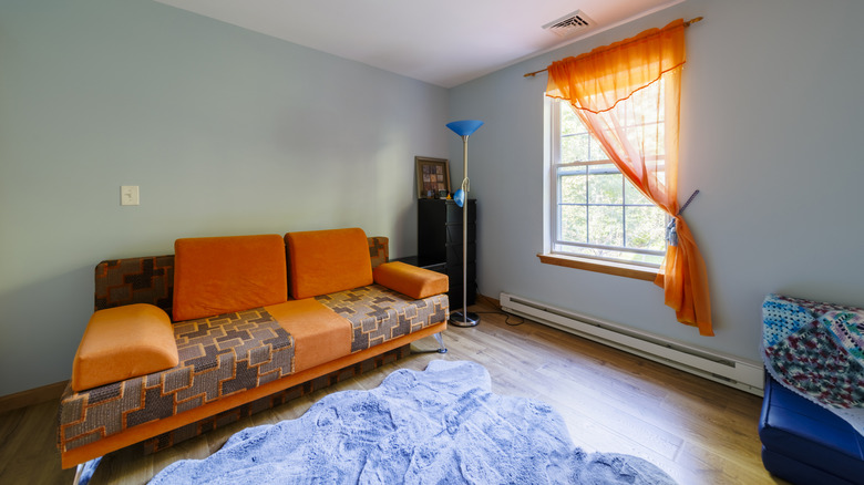 A high contrast room with bright orange couch, orange window curtains, blue lamps, and a blue rug