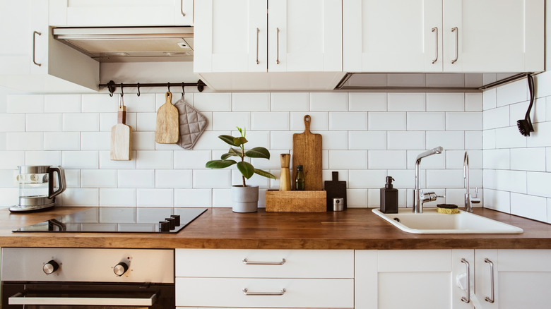 Modern kitchen with white cabinets, brass hardware, white tiles and wood counter top