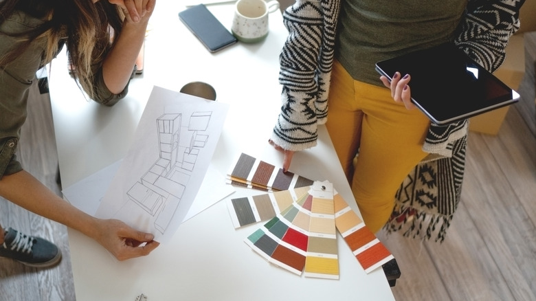 Two women look at paint samples on a table with a kitchen blueprint