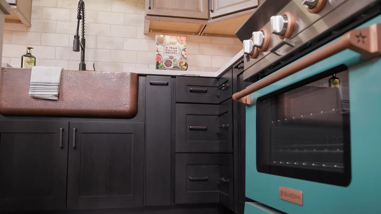Kitchen with black cabinets, a teal oven, and copper accents