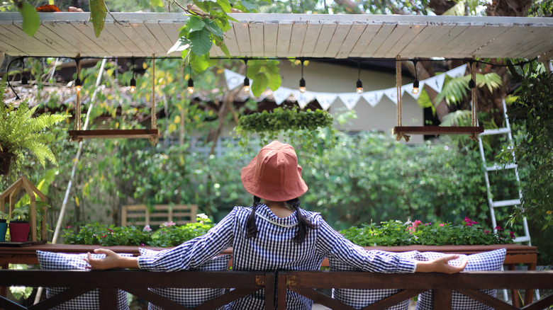 A person relaxing in a garden surrounded by shrubs, trees, and vines