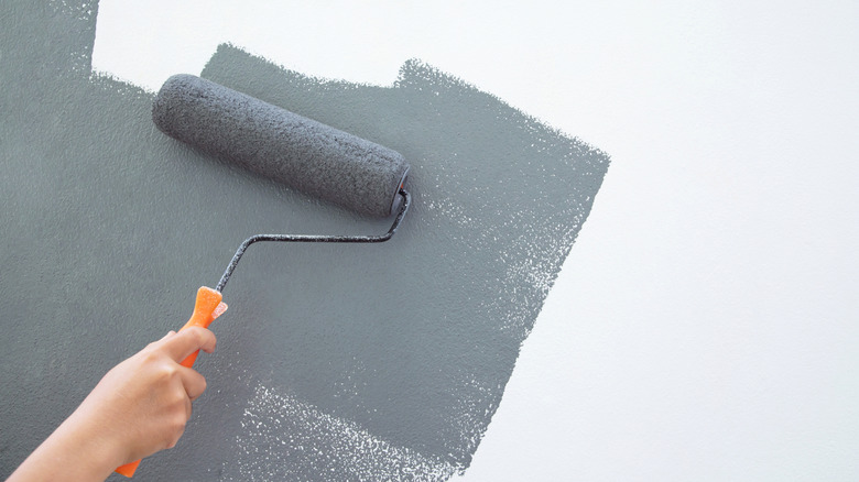 Hand rolling gray paint onto a white wall