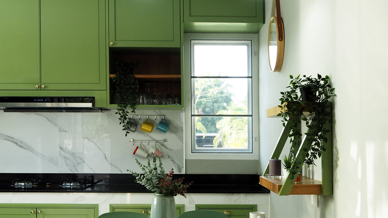 Kitchen with cabinets and accents painted in warm green, with various pieces of greenery and contrasting elements like white and black marble