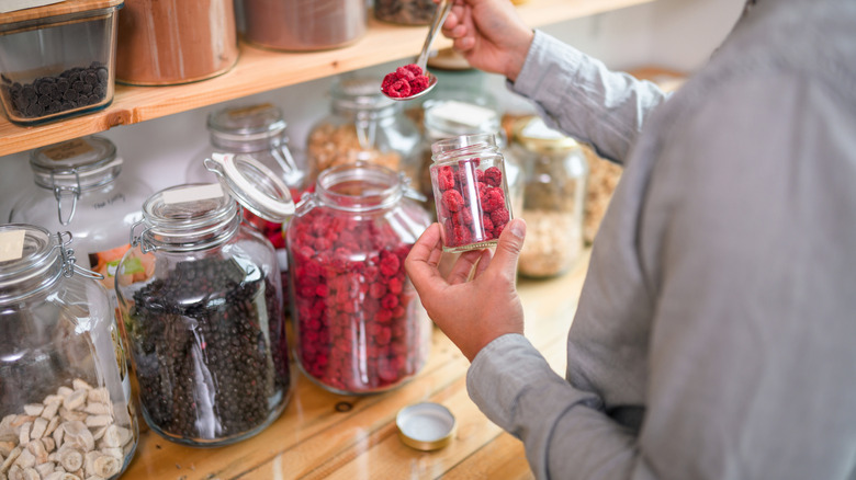 a person adding berries to a jar from a larger jar