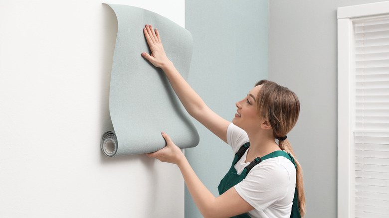 Woman hanging wallpaper on wall