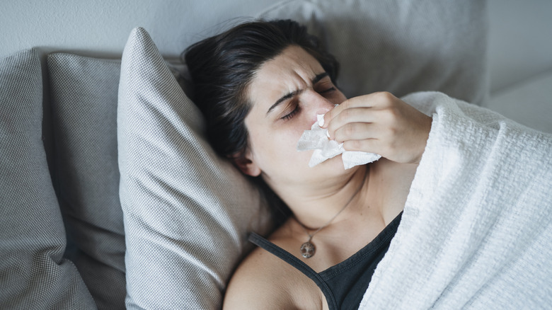 Close up of woman on couch blowing nose into tissue