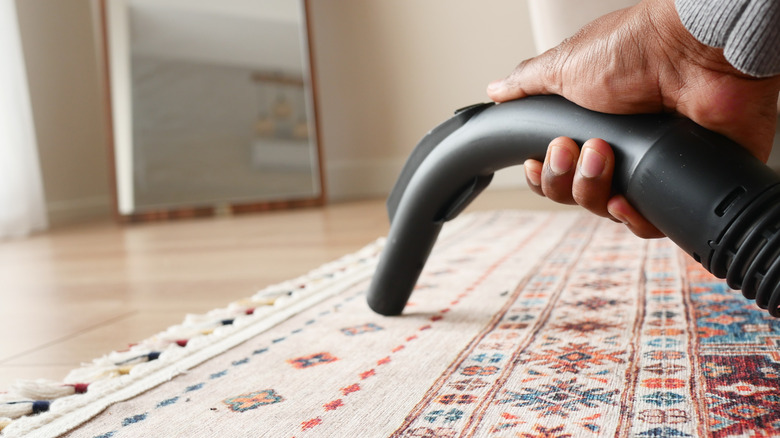 Man using nozzle attachment to vacuum a rug