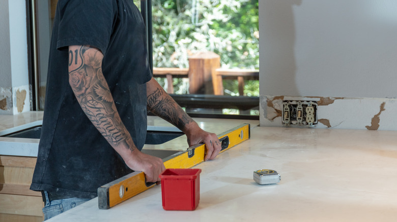 A man with tattoos in a black shirt measuring a level countertop