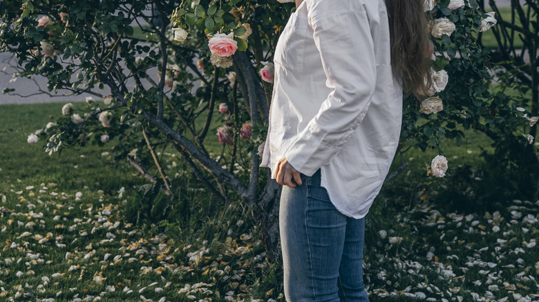 a woman smells a thriving rose bush