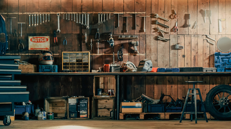 A neatly organized garage workshop with tools hanging on a wooden wall and shelves filled with boxed and equipment