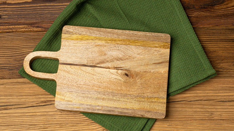 A wood cutting board on top of a green dish towel