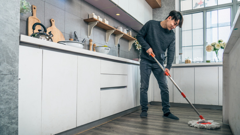 A smiling Asian man mops his kitchen floor.