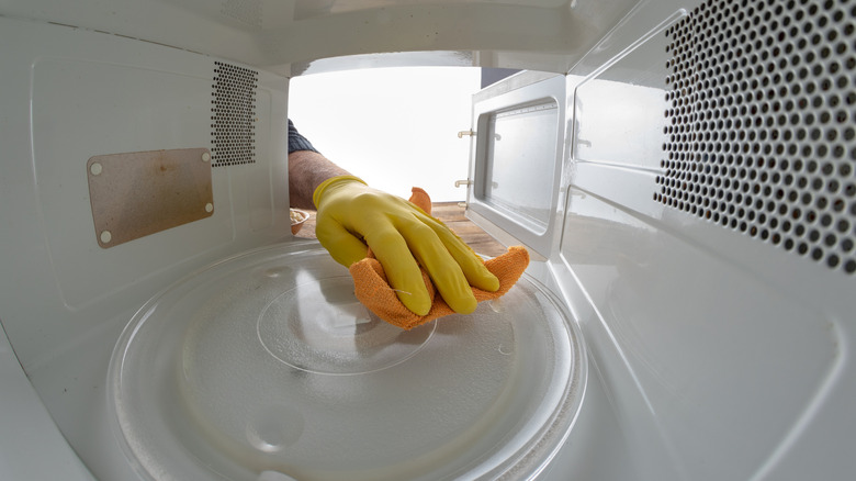 hand cleaning the inside of a microwave