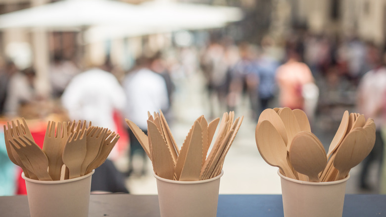 Cups full of disposable wooden cutlery are available for diners at an outdoor cafe.