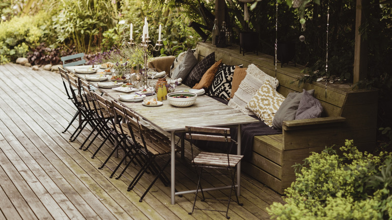 A table, chairs, and bench covered in pillows on a deck set for a meal.