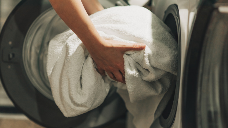 Hands loading a white towel into an open washing machine